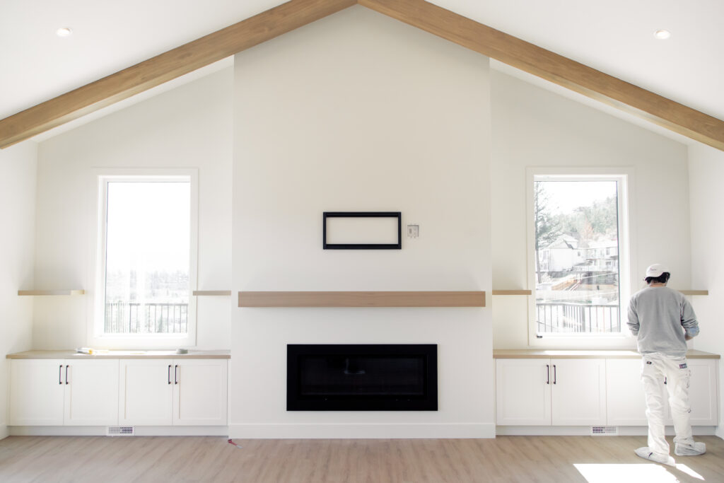 Bright, newly rebuilt living room with vaulted ceiling, modern fireplace, built-in cabinets, and two tall windows.